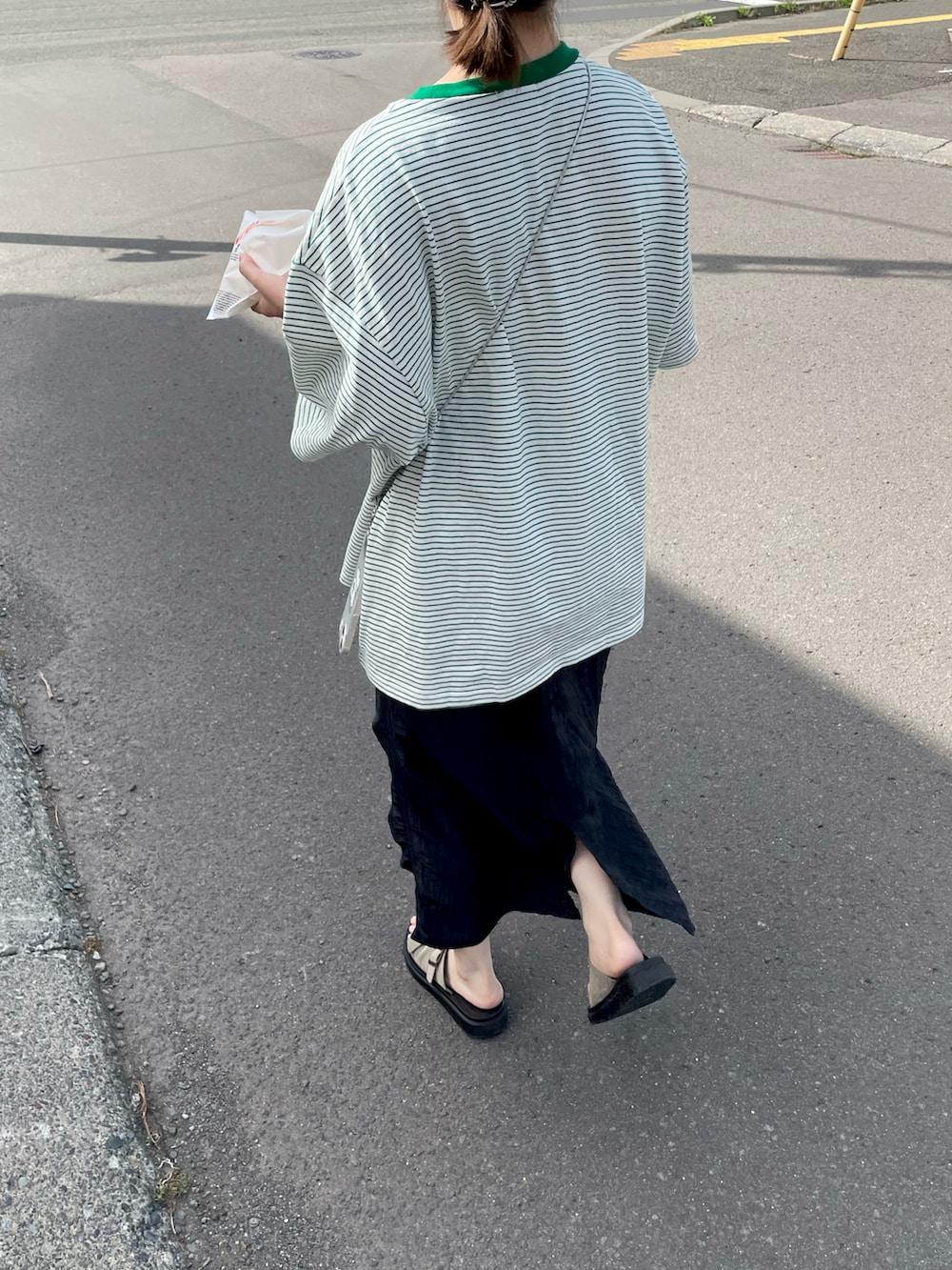 グリーン系のTシャツ/カットソー、ブラック系のスカート、ベージュ系のサンダルを着用したレディースの秋コーディネートの2枚目の写真