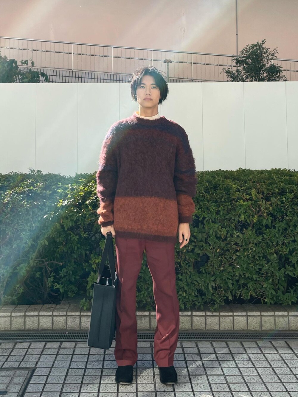 オレンジ系のニット/セーター、ブラウン系のスラックス、ブラック系のトートバッグを着用したメンズの冬コーディネートの5枚目の写真