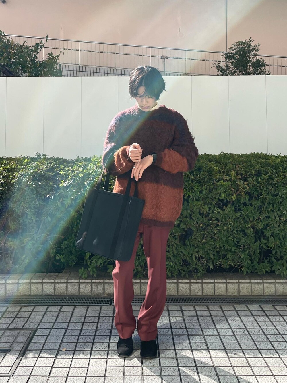 オレンジ系のニット/セーター、ブラウン系のスラックス、ブラック系のトートバッグを着用したメンズの冬コーディネートの2枚目の写真