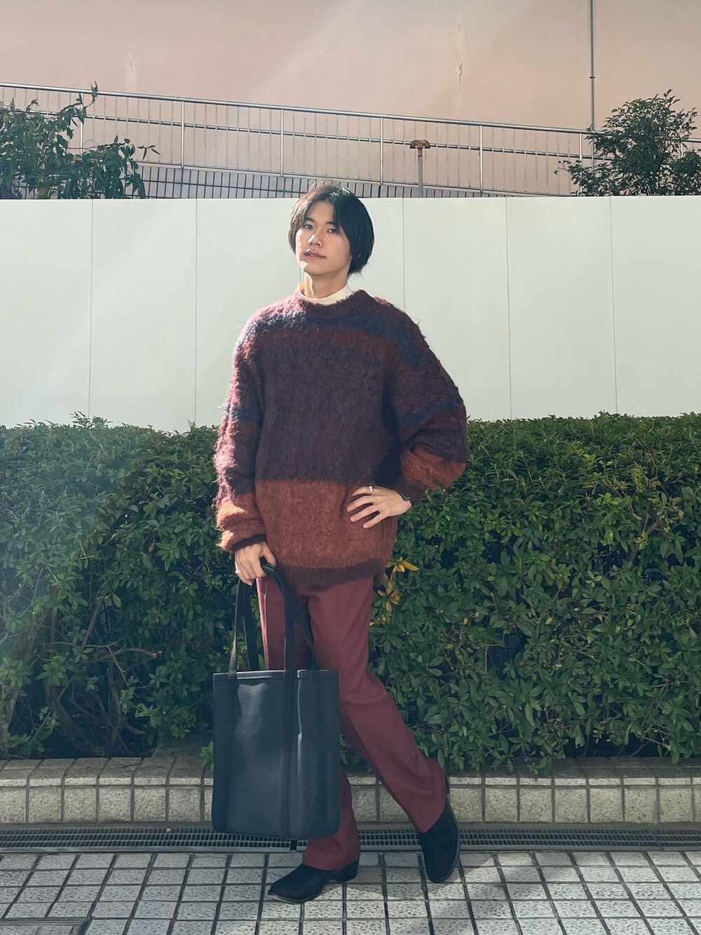 オレンジ系のニット/セーター、ブラウン系のスラックス、ブラック系のトートバッグを着用したメンズの冬コーディネートの4枚目の写真