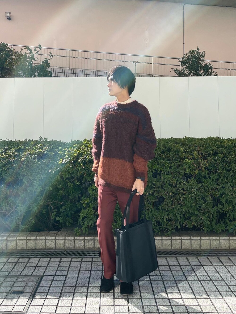 オレンジ系のニット/セーター、ブラウン系のスラックス、ブラック系のトートバッグを着用したメンズの冬コーディネートの3枚目の写真