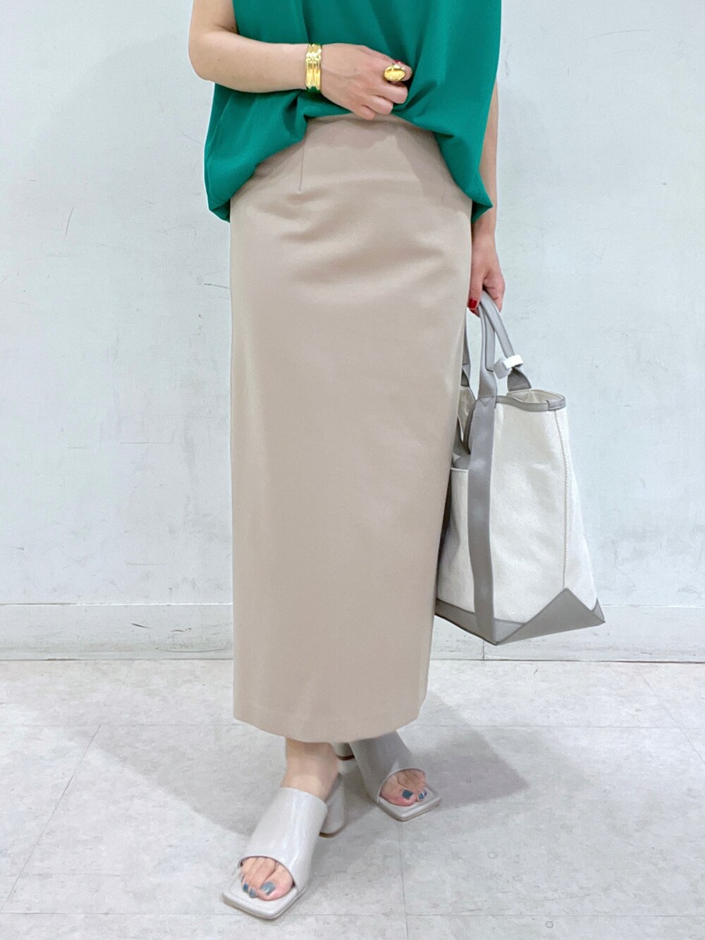 グリーン系のニット/セーター、グレー系のトートバッグ、ベージュ系のスカートを着用したレディースの春コーディネートの5枚目の写真