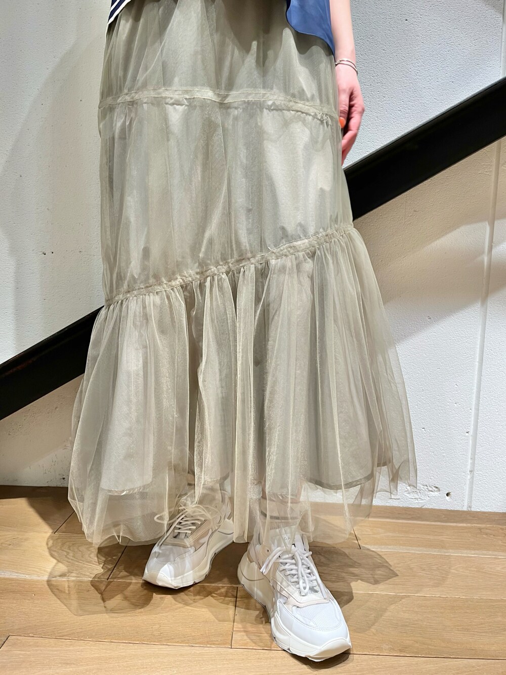 グリーン系のトップス、ゴールド系のスカート、ホワイト系のスニーカーを着用したレディースの春コーディネートの2枚目の写真