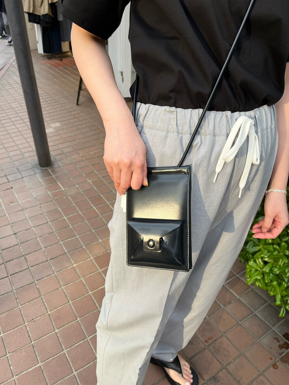 ブラック系のショルダーバッグ、ブラック系のTシャツ/カットソー、グレー系のパンツを着用したレディースの春コーディネートの3枚目の写真
