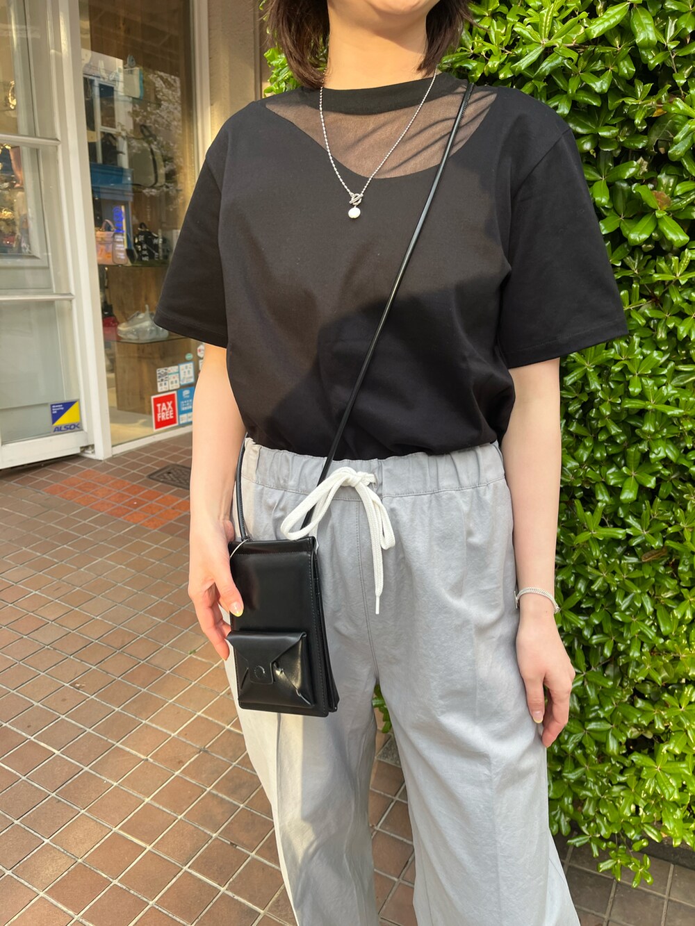 ブラック系のショルダーバッグ、ブラック系のTシャツ/カットソー、グレー系のパンツを着用したレディースの春コーディネートの2枚目の写真