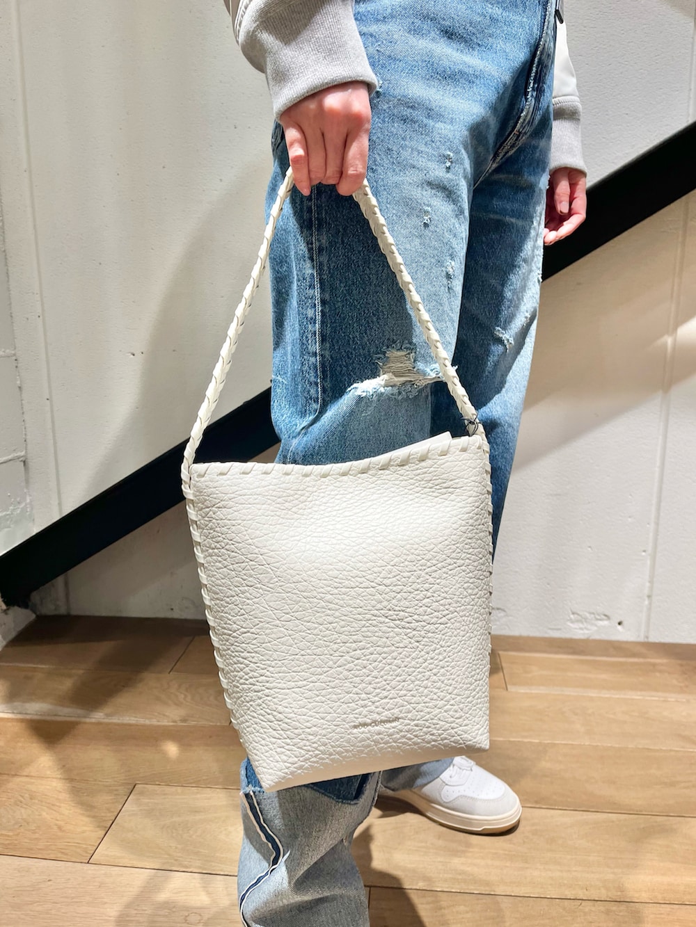 ホワイト系のトートバッグ、グレー系のブルゾン、ブルー系のデニムパンツを着用したレディースの春コーディネートの2枚目の写真