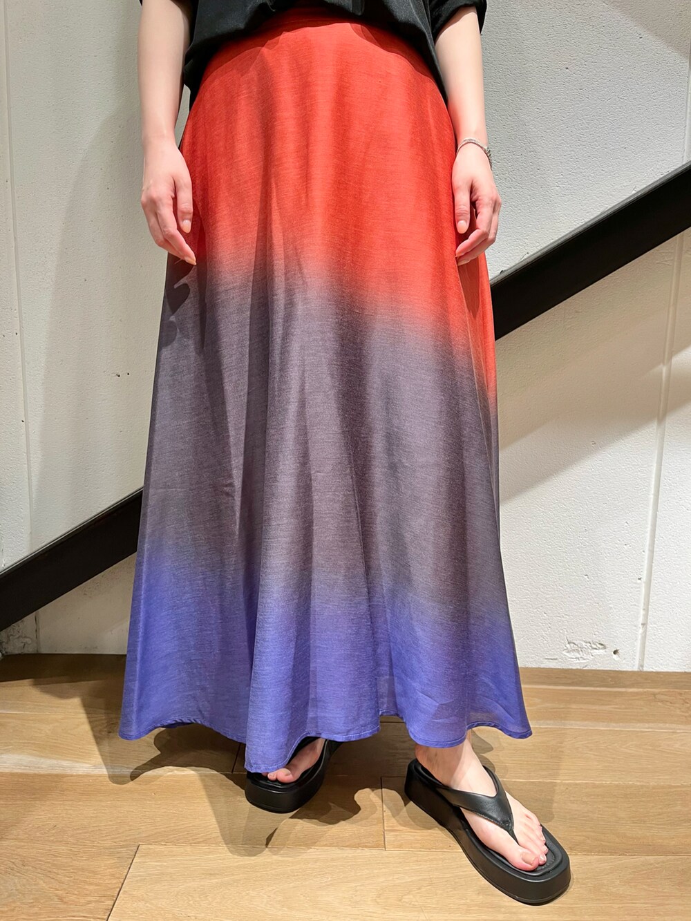 ブラック系のトップス、オレンジ系のスカート、ブラック系のサンダルを着用したレディースの夏コーディネートの2枚目の写真