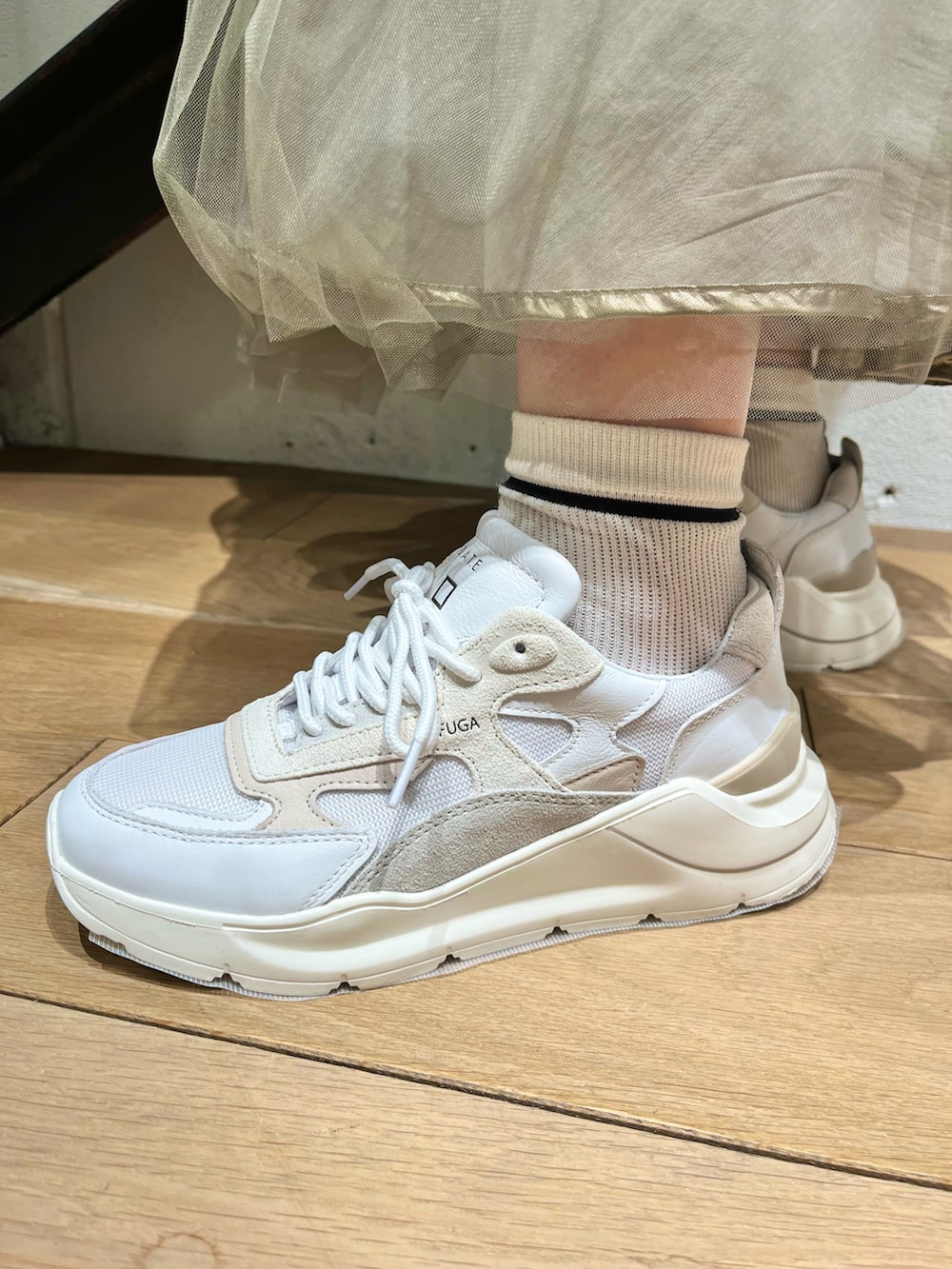 グリーン系のトップス、ゴールド系のスカート、ホワイト系のスニーカーを着用したレディースの春コーディネートの3枚目の写真