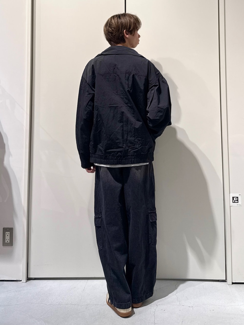 ブラック系のナイロンジャケット、グレー系のニット/セーター、ブラック系のカーゴパンツを着用したメンズの春コーディネートの2枚目の写真