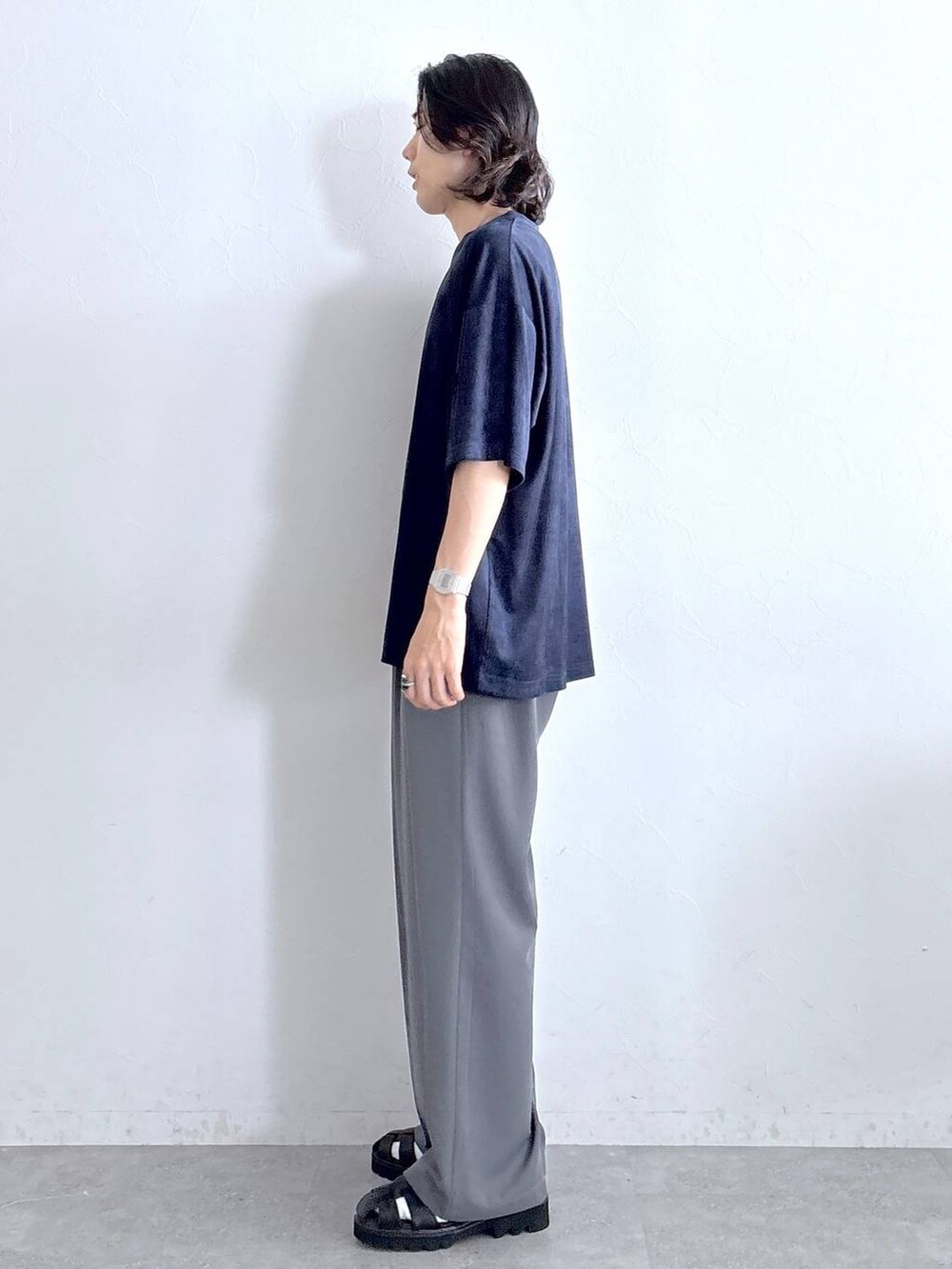 グレー系のスラックス、ブラック系のサンダル、ブルー系のTシャツ/カットソーを着用したメンズの夏コーディネートの3枚目の写真