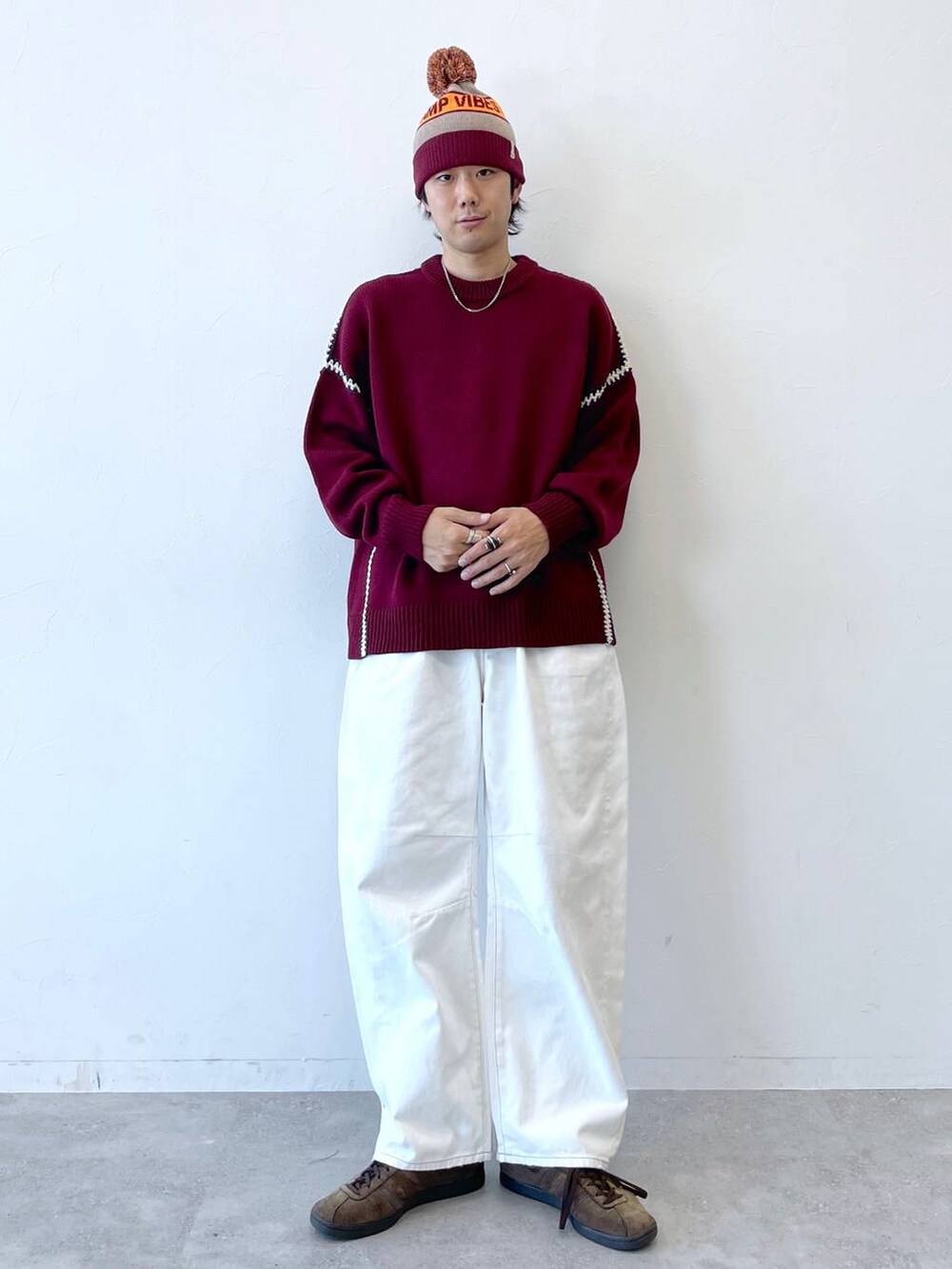 レッド系のニット/セーター、ホワイト系のデニムパンツ、グレー系のニットキャップ/ビーニーを着用したメンズの秋コーディネートの2枚目の写真