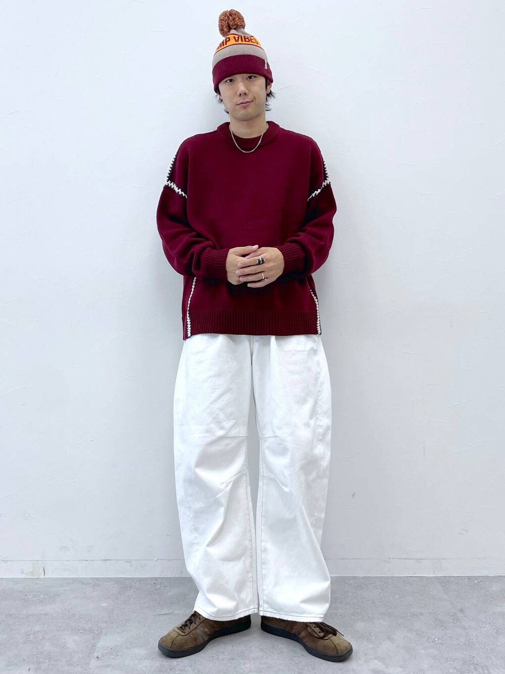 レッド系のニット/セーター、ホワイト系のデニムパンツ、グレー系のニットキャップ/ビーニーを着用したメンズの秋コーディネートの3枚目の写真