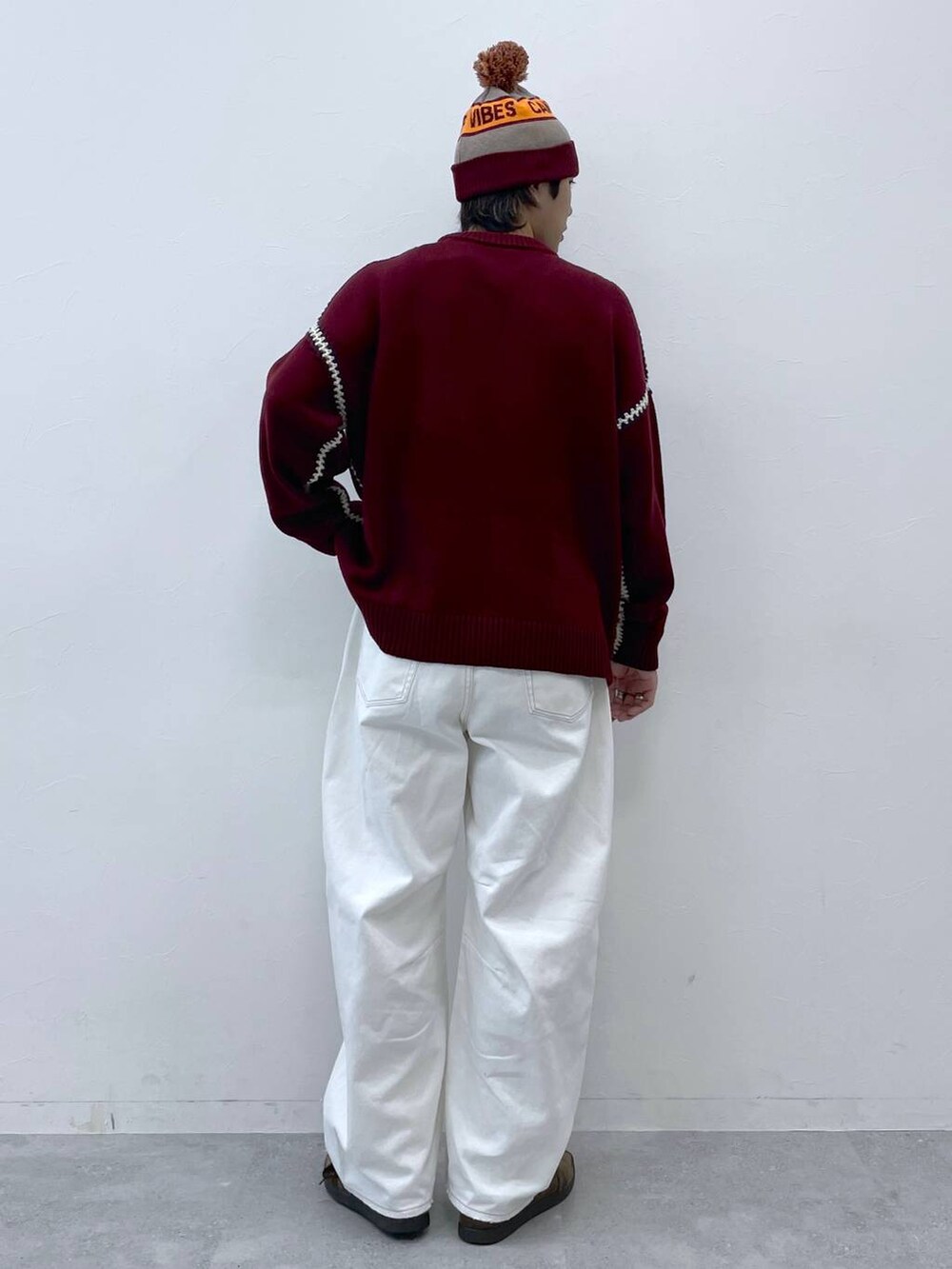 レッド系のニット/セーター、ホワイト系のデニムパンツ、グレー系のニットキャップ/ビーニーを着用したメンズの秋コーディネートの6枚目の写真