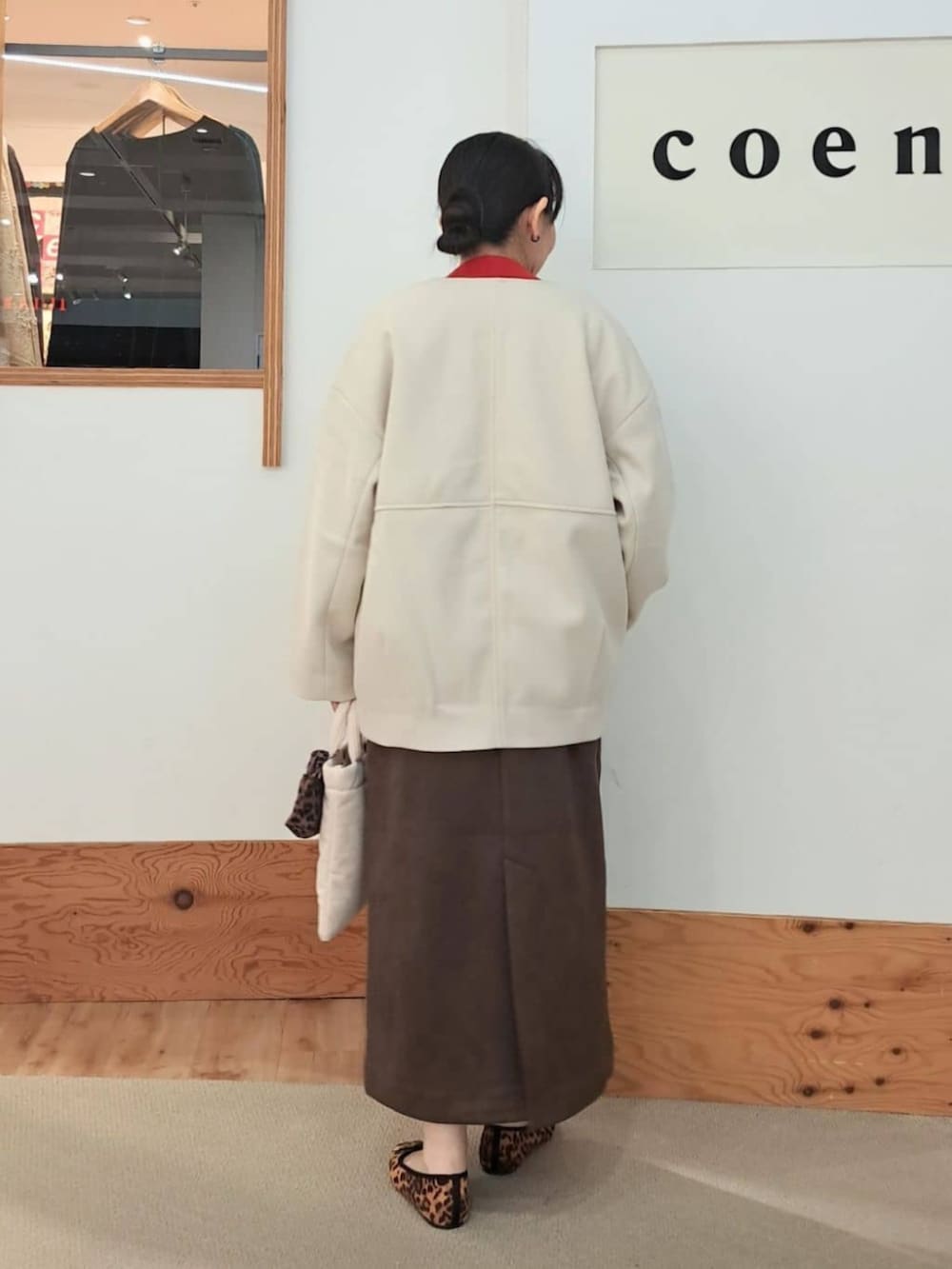 ベージュ系のノーカラーコート、ブラウン系のジャンパースカート、ベージュ系のショルダーバッグを着用したレディースの秋コーディネートの3枚目の写真