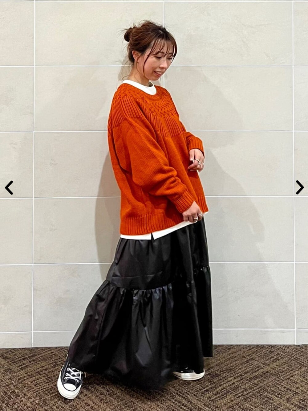 オレンジ系のニット/セーター、ブラック系のスカートを着用したレディースの秋コーディネートの2枚目の写真