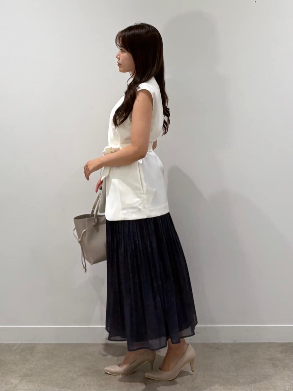 ホワイト系のベスト、ブルー系のスカート、ベージュ系のパンプスを着用したレディースの夏コーディネートの2枚目の写真