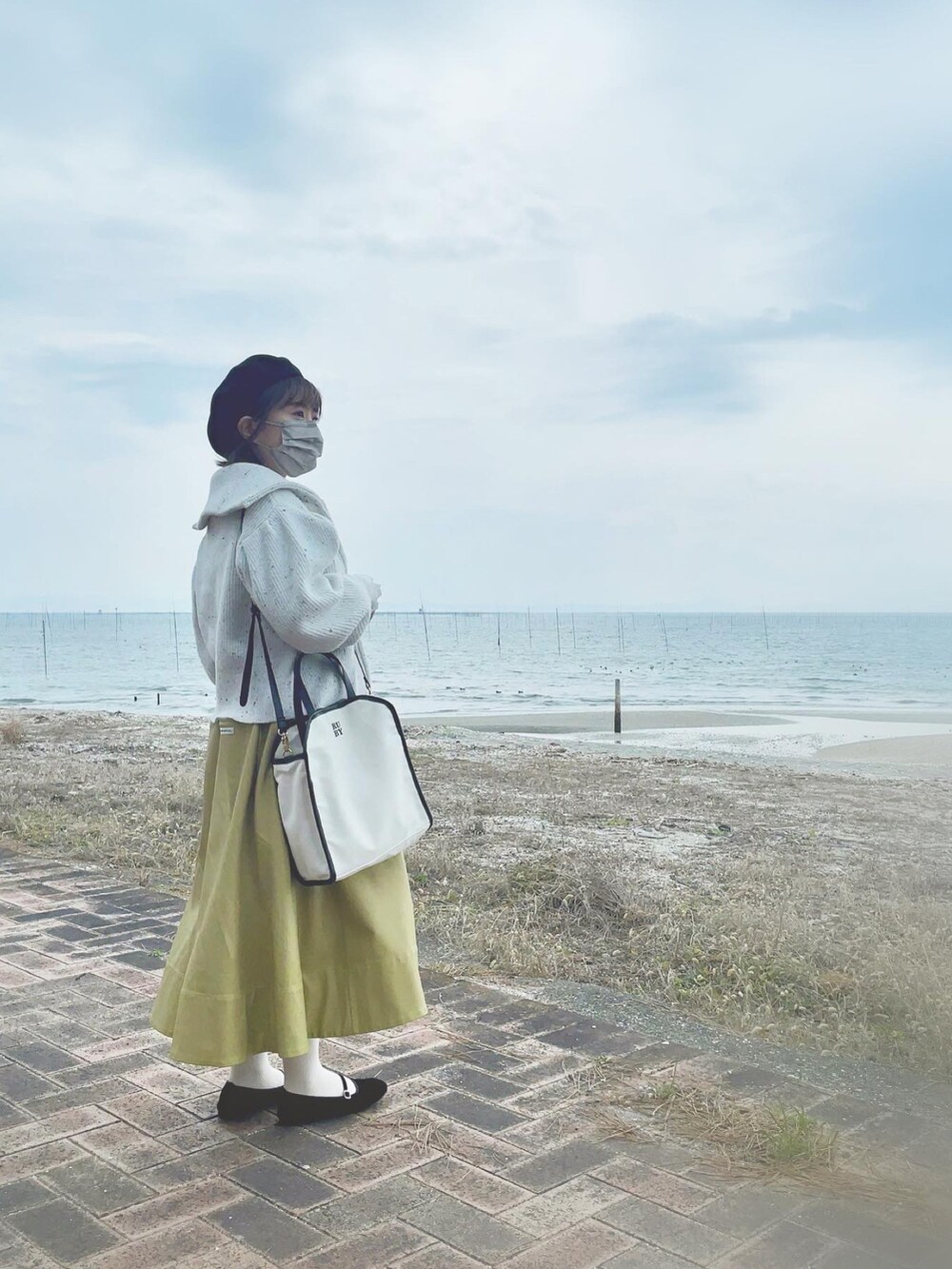 イエロー系のジャンパースカート、ブラック系のハンチング/ベレー帽を着用したレディースの春コーディネートの2枚目の写真