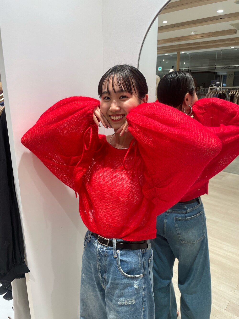 レッド系のニット/セーター、ブルー系のデニムパンツを着用したレディースの秋コーディネートの2枚目の写真