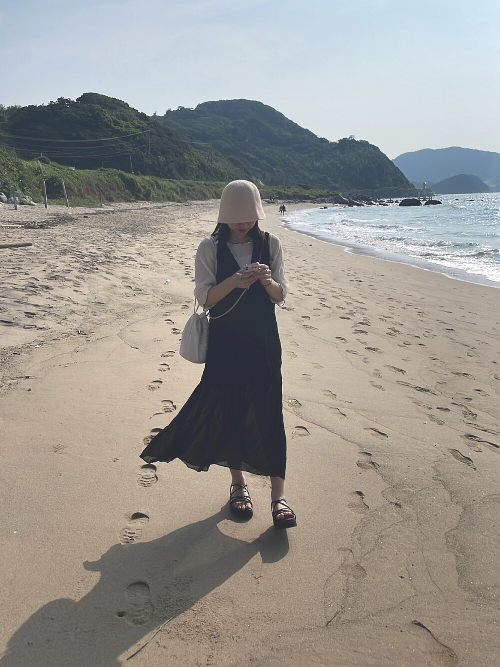 ブラック系のワンピース、ブラック系のサンダル、ベージュ系のハンドバッグを着用したレディースの秋コーディネートの2枚目の写真