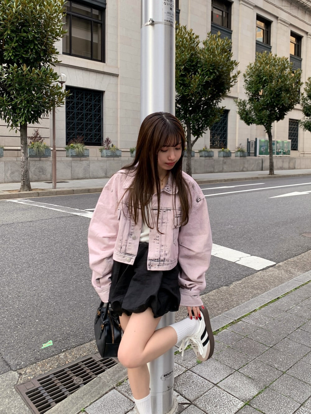 ピンク系のデニムジャケット、ホワイト系のスニーカー、ブラック系のハンドバッグを着用したレディースの春コーディネートの2枚目の写真