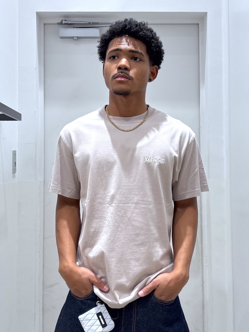 ベージュ系のTシャツ/カットソー、ブルー系のデニムパンツ、ホワイト系のコインケースを着用したメンズの夏コーディネートの3枚目の写真