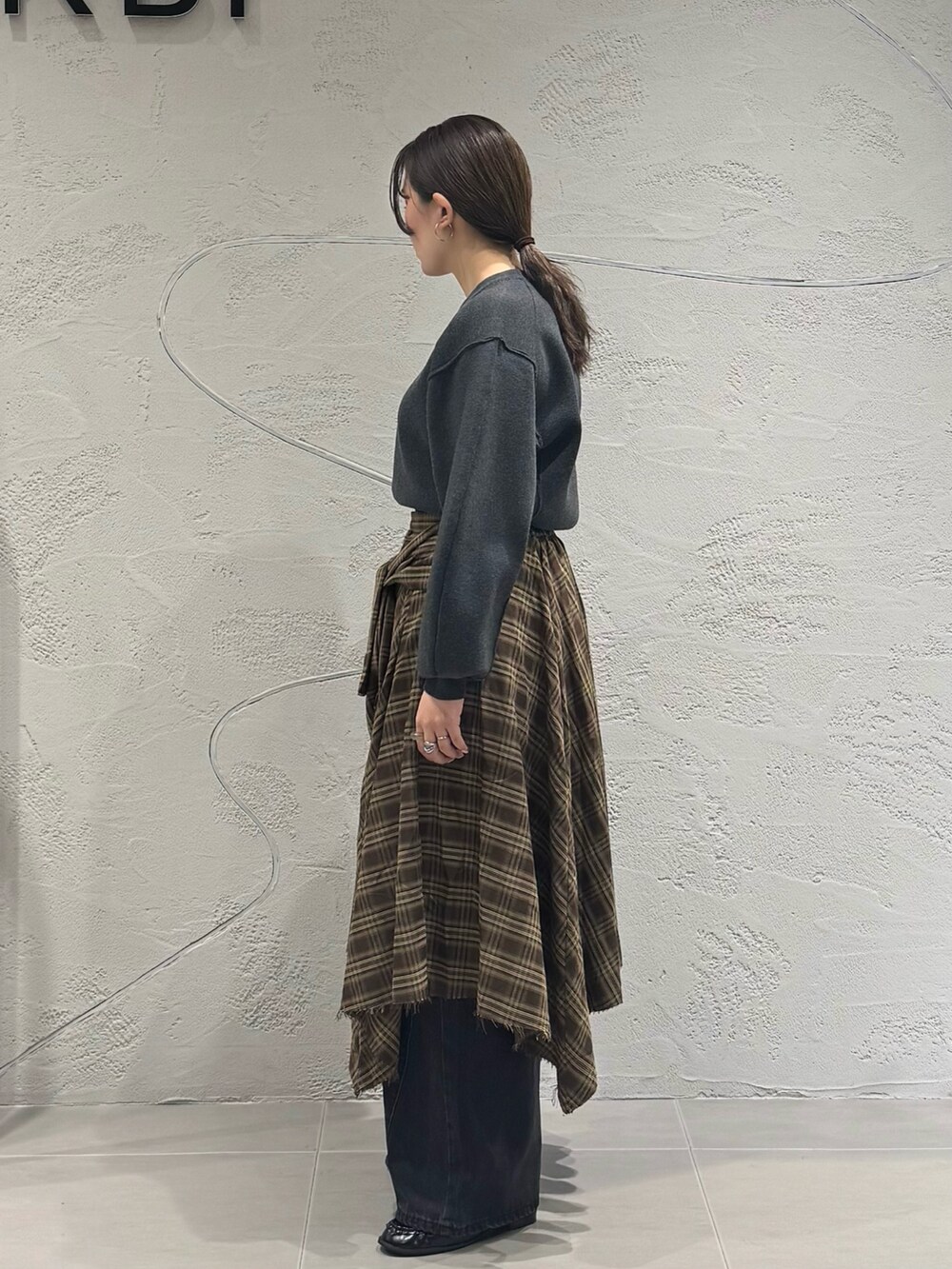 ブラック系のデニムパンツ、ブラウン系のスカート、グレー系のニット/セーターを着用したレディースの秋コーディネートの7枚目の写真