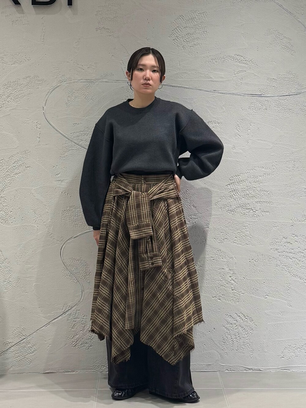 ブラック系のデニムパンツ、ブラウン系のスカート、グレー系のニット/セーターを着用したレディースの秋コーディネートの2枚目の写真