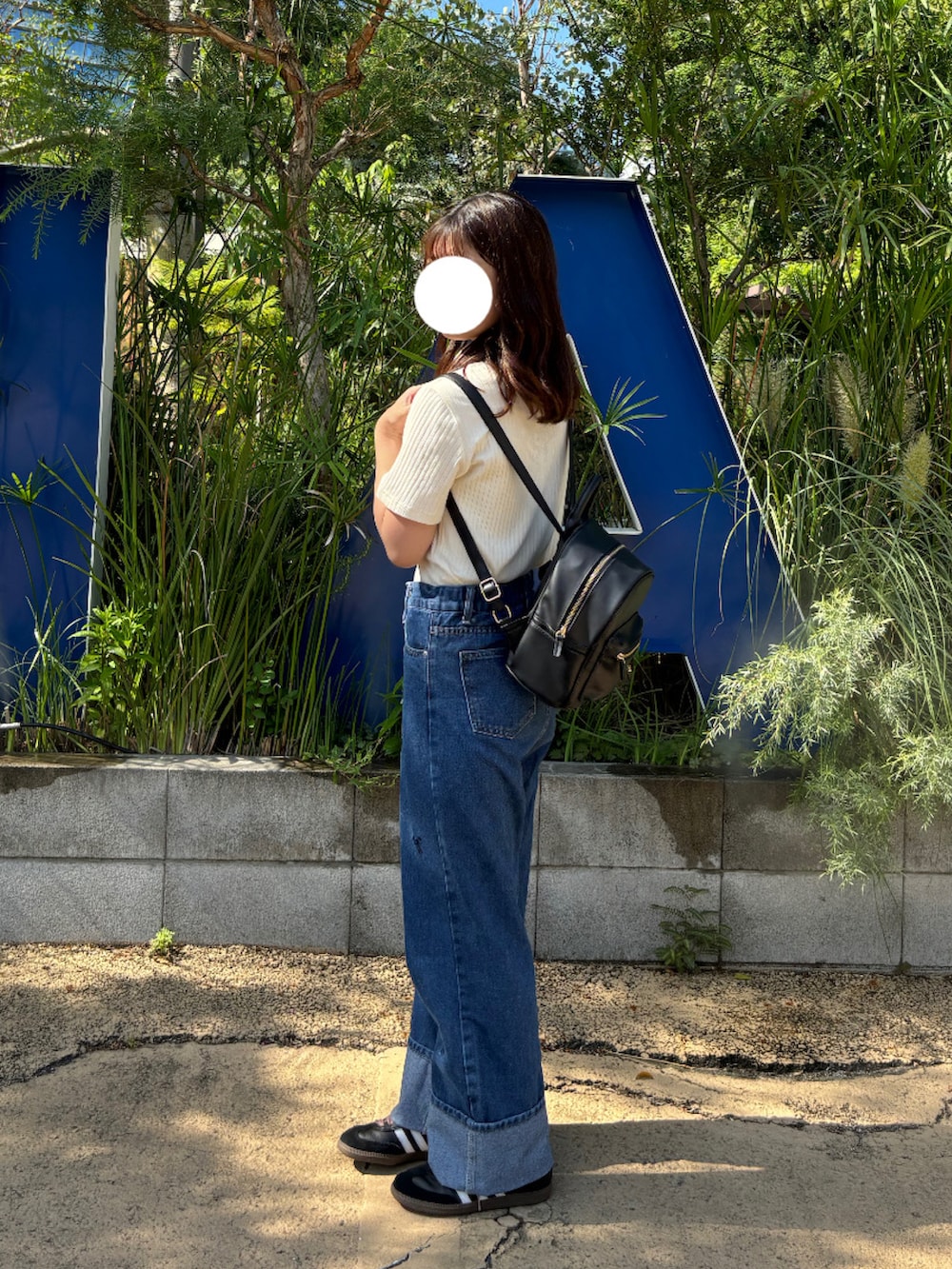 ブルー系のデニムパンツ、ベージュ系のポロシャツ、ブラック系のスニーカーを着用したレディースの夏コーディネートの2枚目の写真