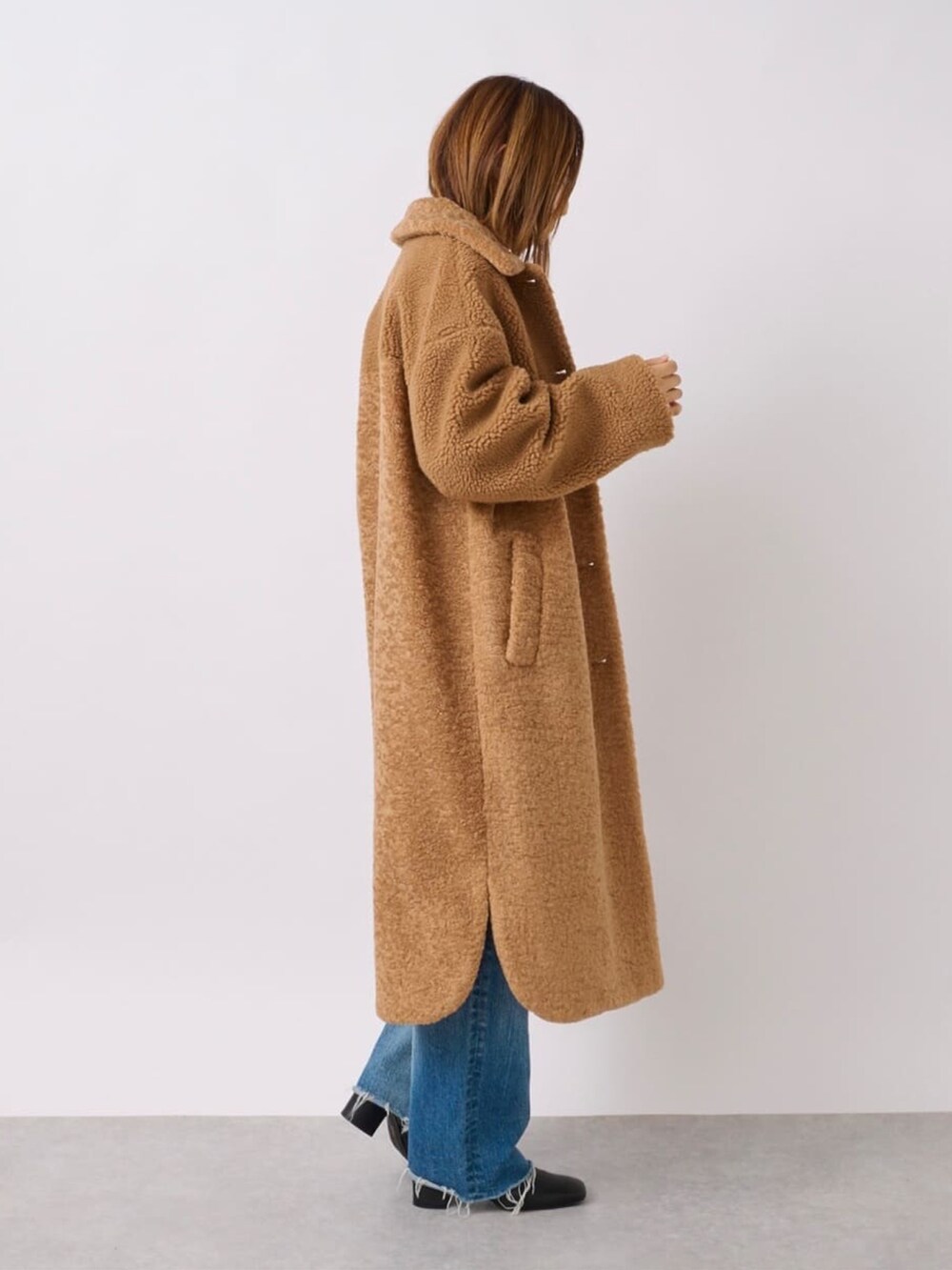 イエロー系のステンカラーコート、ブラック系のブーツ、ブラック系のショルダーバッグを着用したレディースの冬コーディネートの4枚目の写真