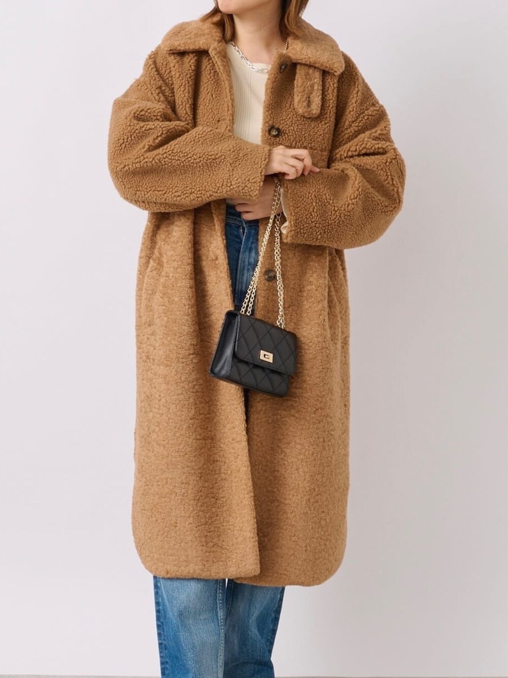 イエロー系のステンカラーコート、ブラック系のブーツ、ブラック系のショルダーバッグを着用したレディースの冬コーディネートの5枚目の写真