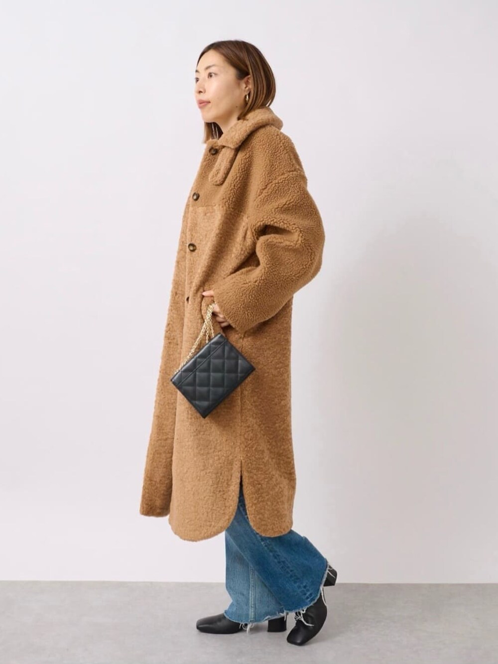 イエロー系のステンカラーコート、ブラック系のブーツ、ブラック系のショルダーバッグを着用したレディースの冬コーディネートの2枚目の写真