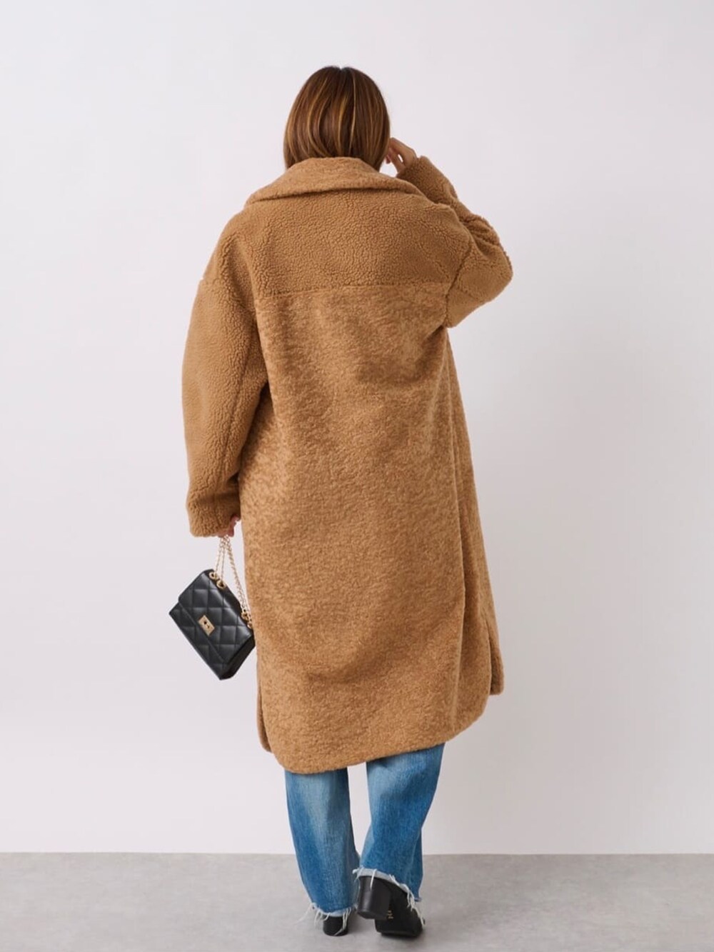 イエロー系のステンカラーコート、ブラック系のブーツ、ブラック系のショルダーバッグを着用したレディースの冬コーディネートの3枚目の写真