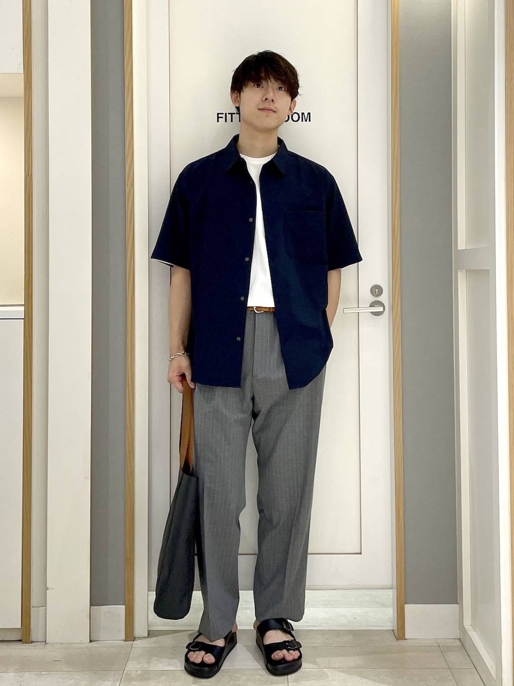 ブラック系のトートバッグ、グレー系のスラックス、ホワイト系のTシャツ/カットソーを着用したメンズの夏コーディネートの2枚目の写真