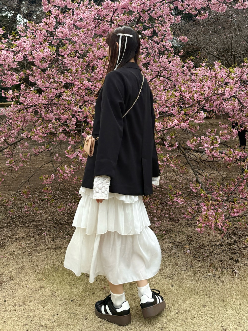 ブラック系のテーラードジャケット、ホワイト系のスカート、ブラック系のスニーカーを着用したレディースの春コーディネートの3枚目の写真
