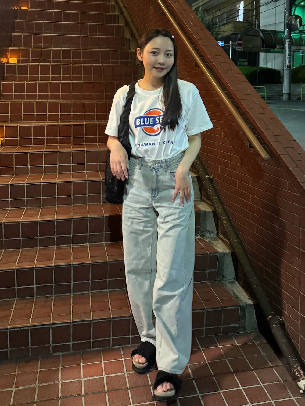 ブラック系のトートバッグ、ブラック系のサンダル、ブルー系のデニムパンツを着用したレディースの夏コーディネートの2枚目の写真