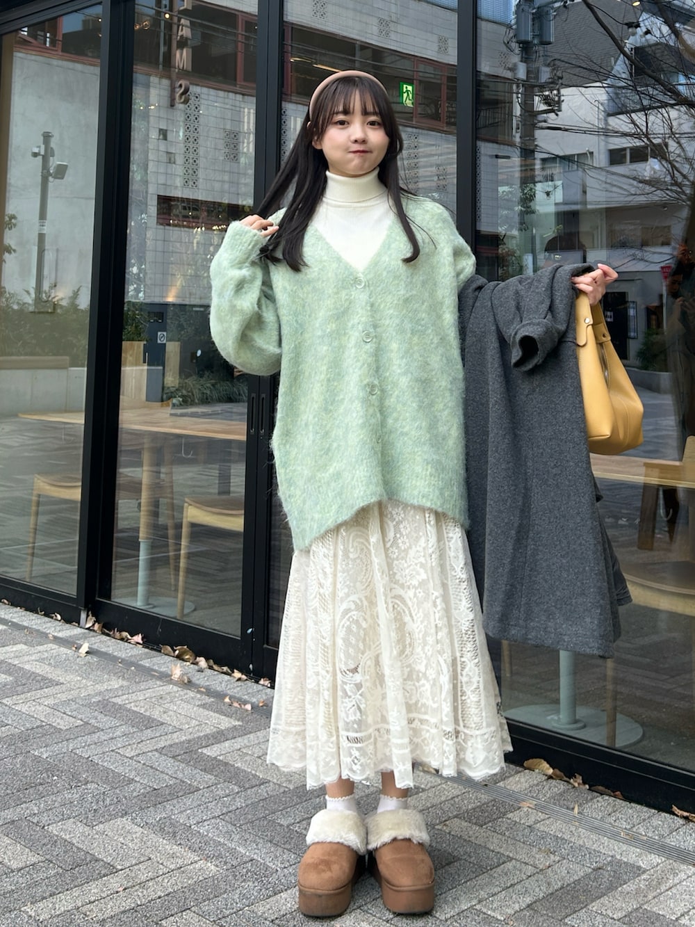 イエロー系のハンドバッグ、ブラック系のステンカラーコート、ベージュ系のスカートを着用したレディースの冬コーディネートの2枚目の写真