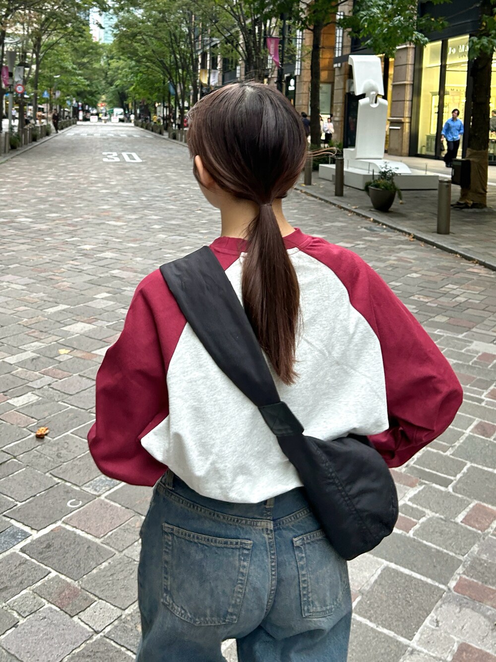 レッド系のTシャツ/カットソー、ブラック系のショルダーバッグ、ブルー系のデニムパンツを着用したレディースの秋コーディネートの5枚目の写真