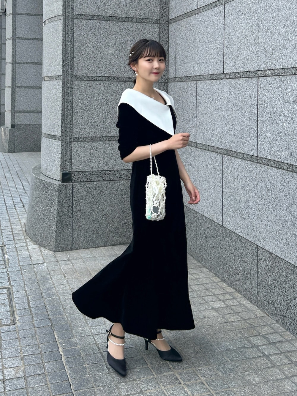 ブラック系のドレス、ホワイト系のハンドバッグ、ブラック系のパンプスを着用したレディースの夏コーディネートの2枚目の写真