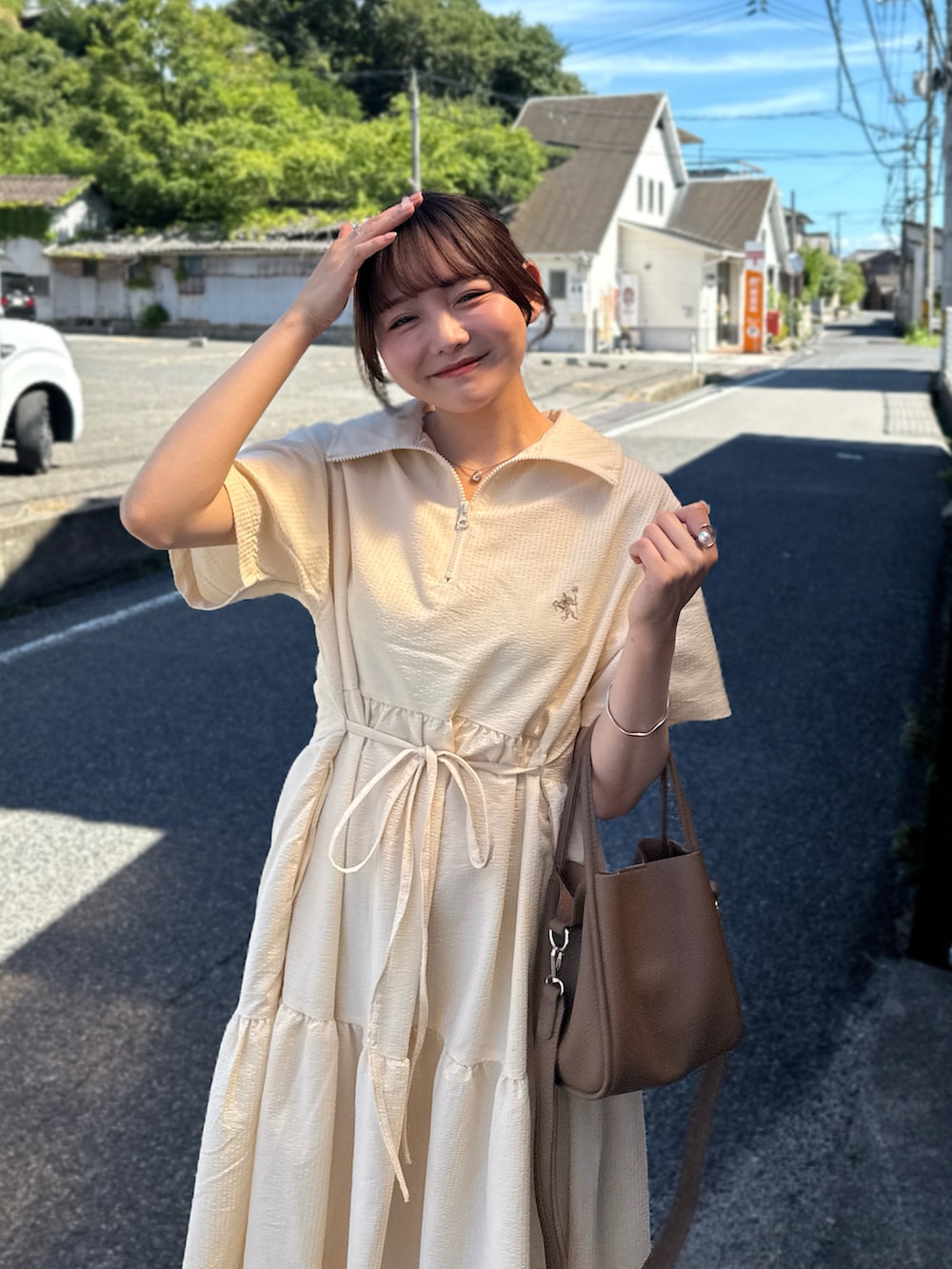 ホワイト系のワンピース、ホワイト系のサンダル、ブラウン系のハンドバッグを着用したレディースの夏コーディネートの2枚目の写真