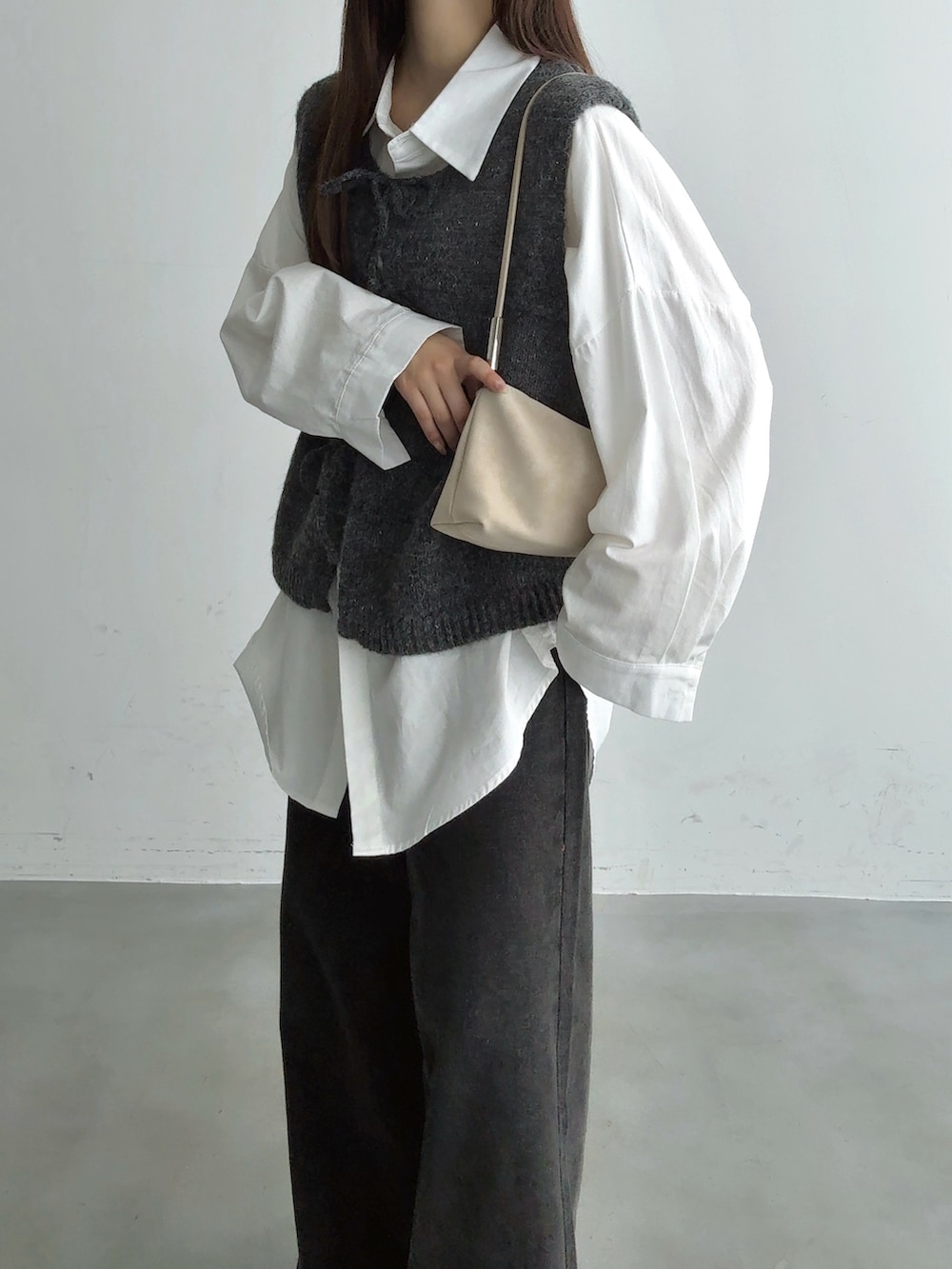 グレー系のベスト、ブラック系のその他パンツ、ホワイト系のショルダーバッグを着用したレディースの秋コーディネートの3枚目の写真