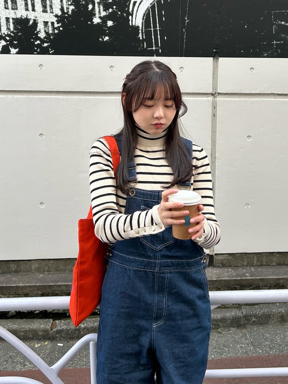 ブルー系のサロペット/オーバーオール、ホワイト系のニット/セーター、オレンジ系のトートバッグを着用したレディースの春コーディネートの5枚目の写真