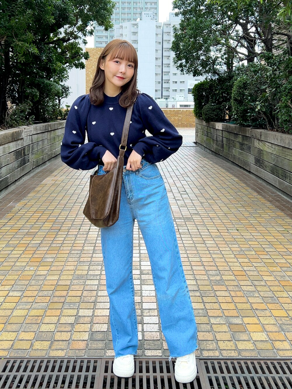 ブルー系のニット/セーター、ブラウン系のショルダーバッグ、ブルー系のデニムパンツを着用したレディースの春コーディネートの2枚目の写真