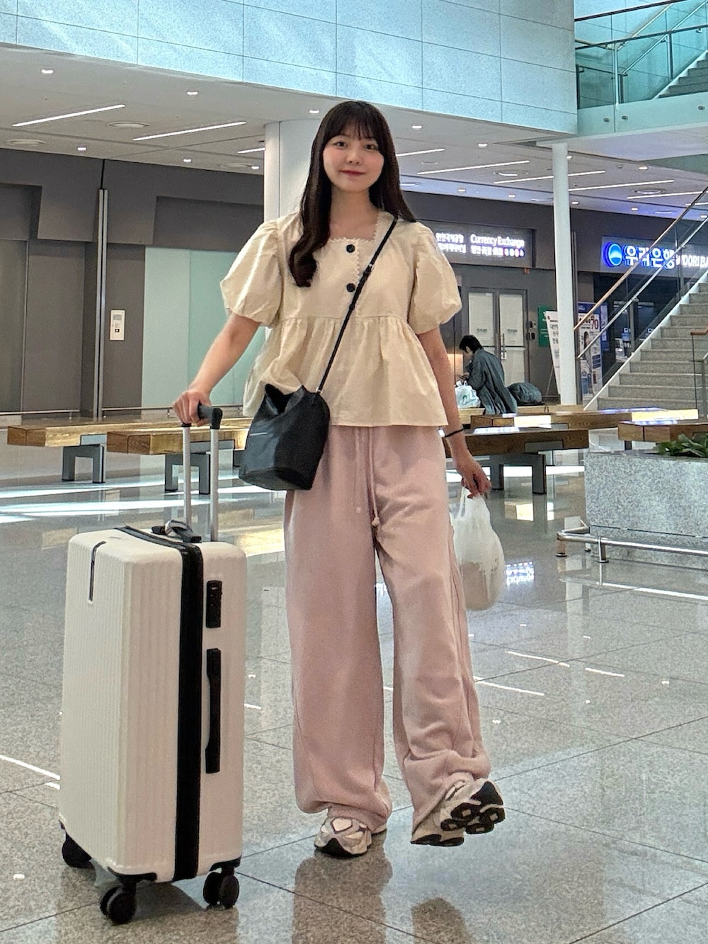ベージュ系のシャツ/ブラウス、ブラック系のショルダーバッグ、ブルー系のデニムパンツを着用したレディースの春コーディネートの2枚目の写真