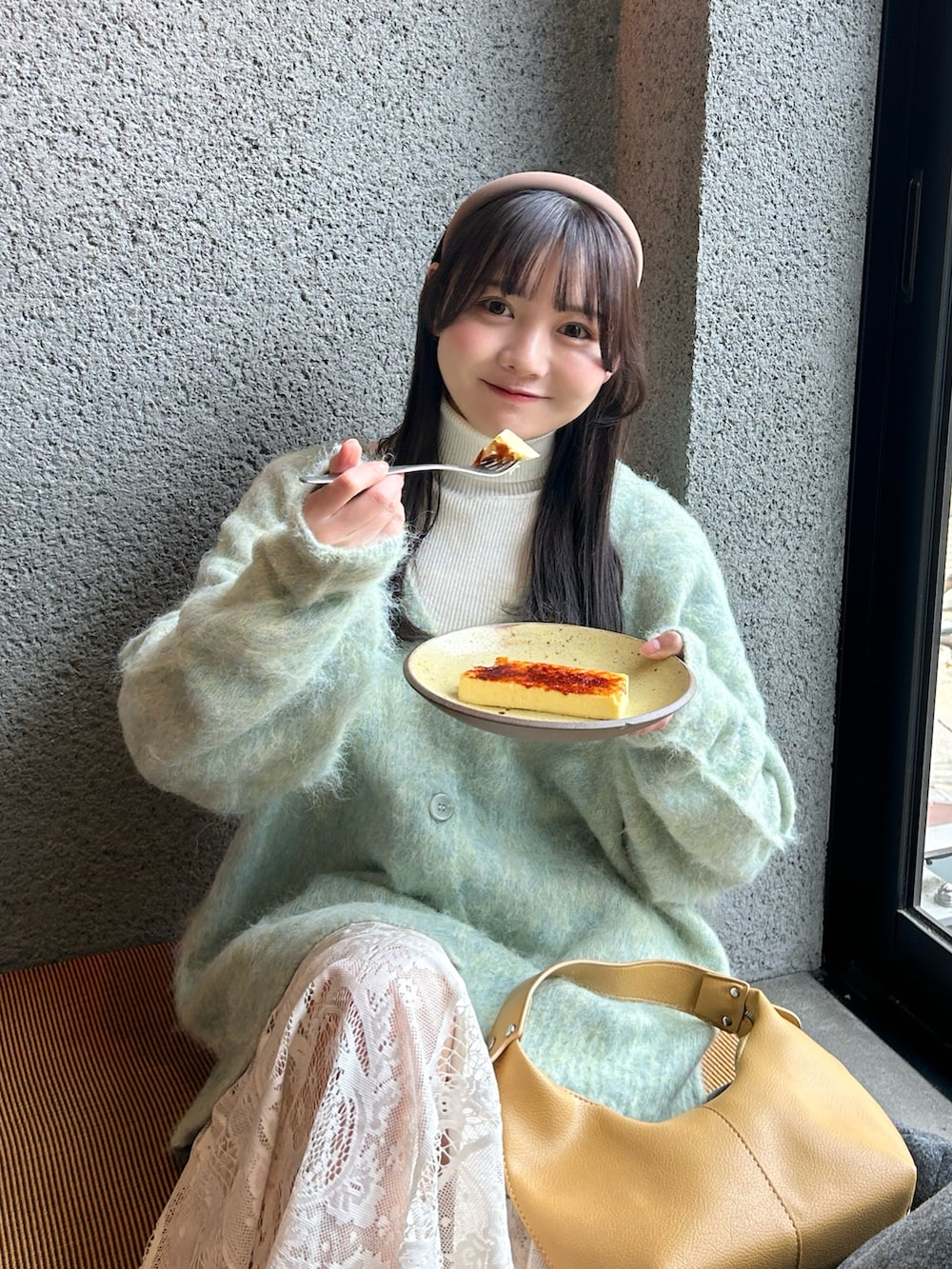 イエロー系のハンドバッグ、ブラック系のステンカラーコート、ベージュ系のスカートを着用したレディースの冬コーディネートの3枚目の写真