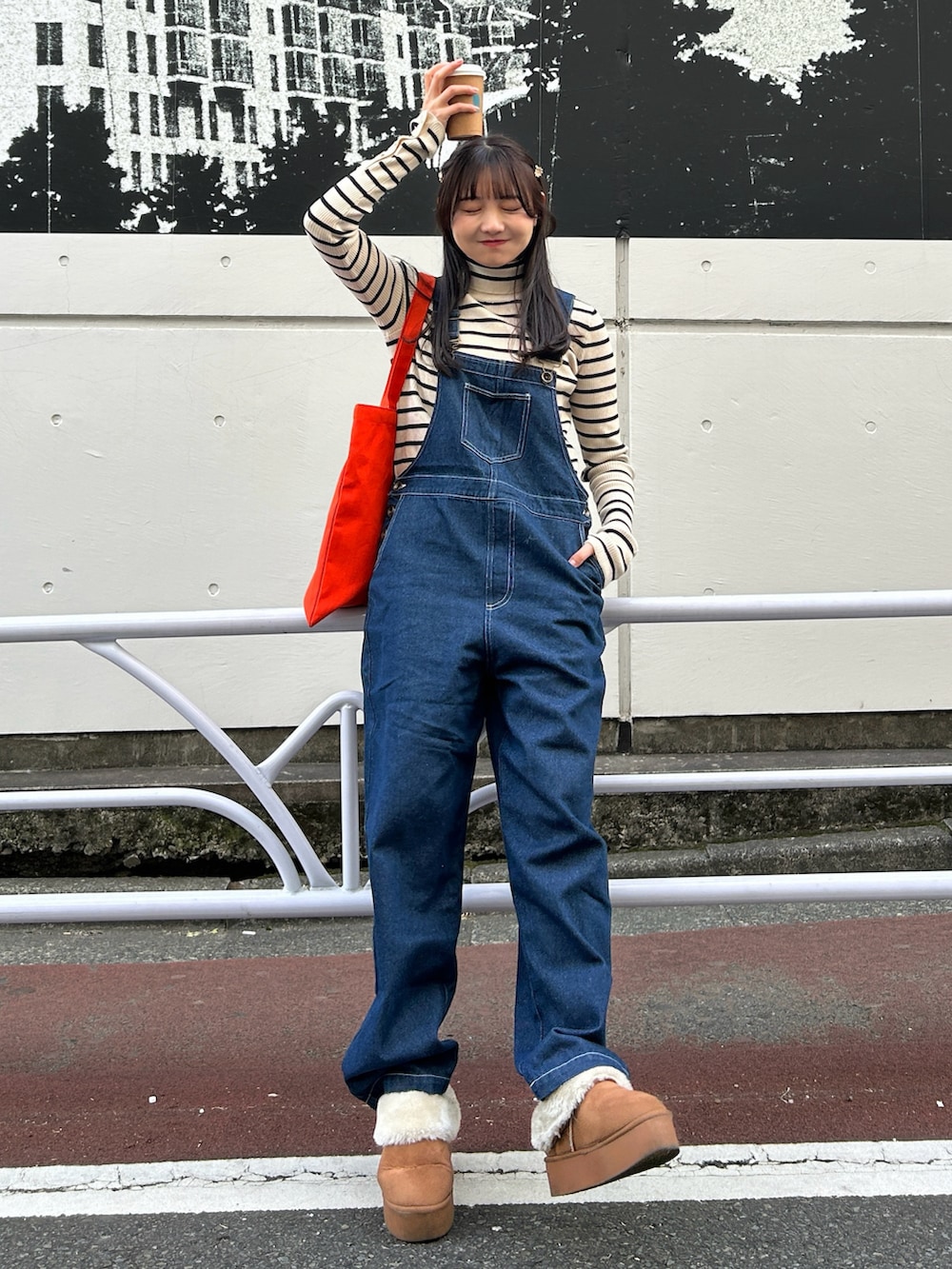 ブラック系のステンカラーコート、ホワイト系のニット/セーター、ブルー系のサロペット/オーバーオールを着用したレディースの冬コーディネートの3枚目の写真