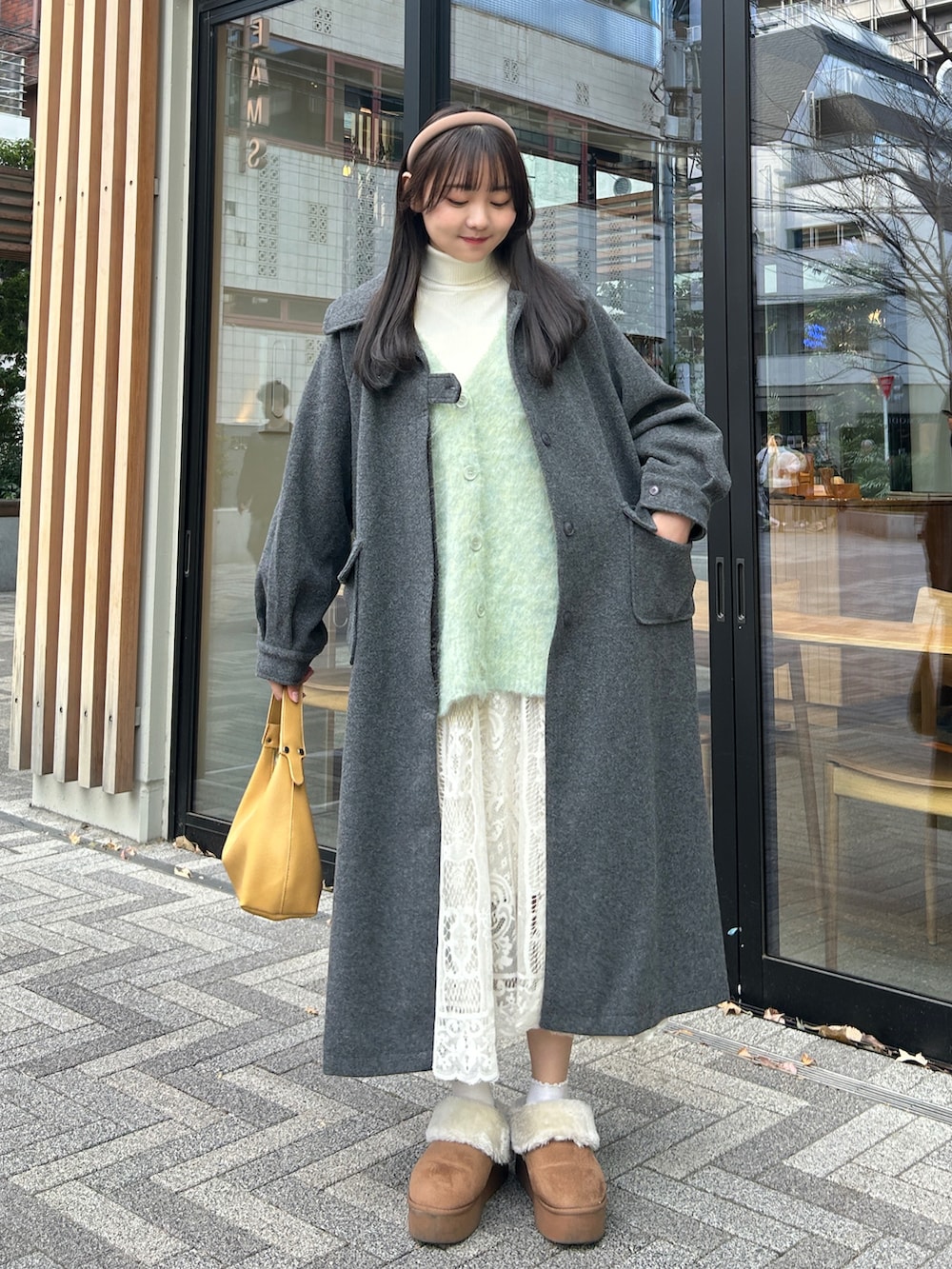 イエロー系のハンドバッグ、ブラック系のステンカラーコート、ベージュ系のスカートを着用したレディースの冬コーディネートの4枚目の写真