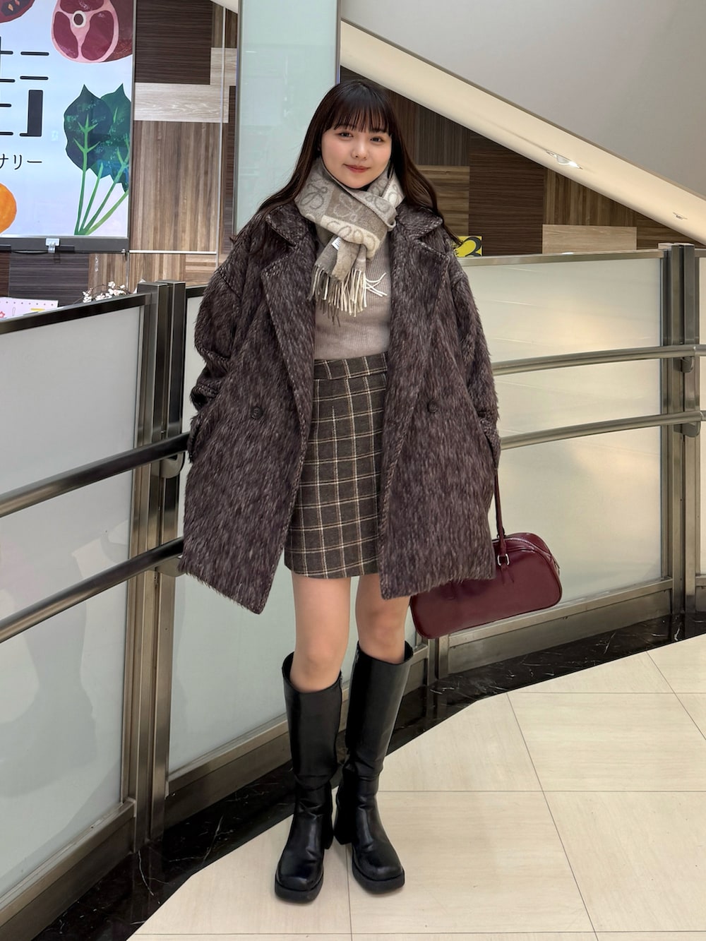 ブラウン系のスカート、レッド系のボストンバッグ、ブラウン系のピーコートを着用したレディースの冬コーディネートの3枚目の写真