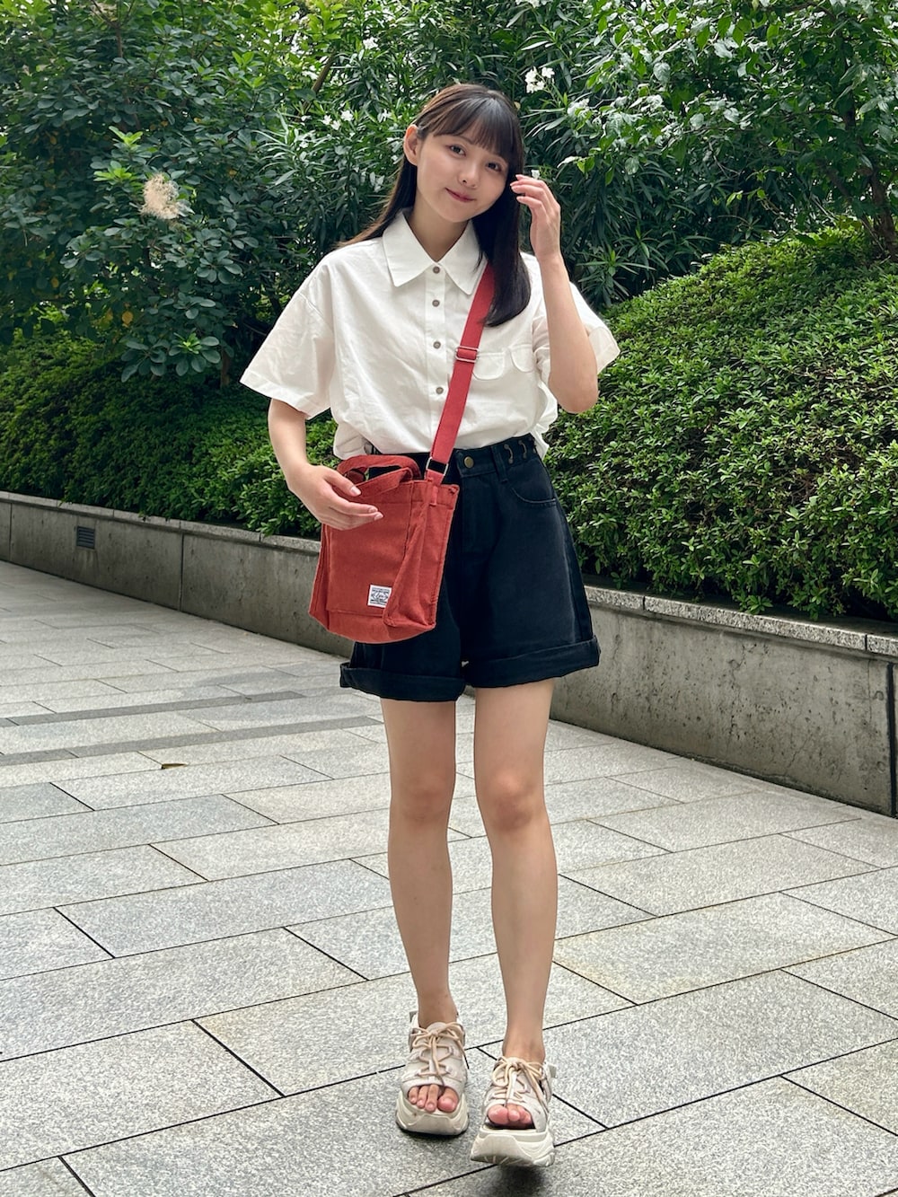 レッド系のショルダーバッグ、ベージュ系のサンダル、ホワイト系のシャツ/ブラウスを着用したレディースの夏コーディネートの2枚目の写真
