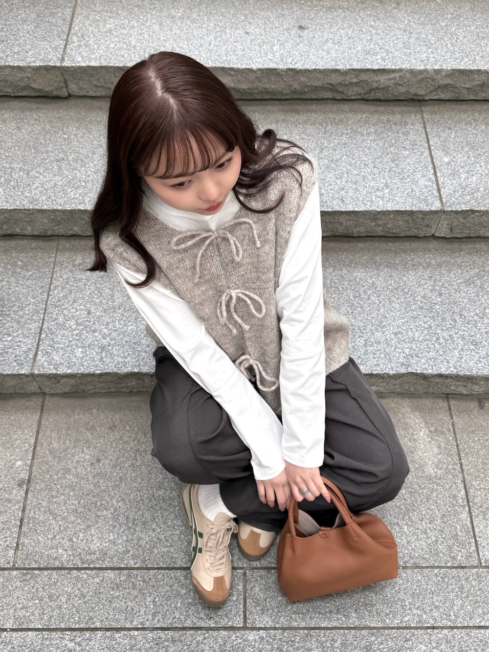 ベージュ系のステンカラーコート、ホワイト系のTシャツ/カットソー、ベージュ系のベストを着用したレディースの冬コーディネートの4枚目の写真