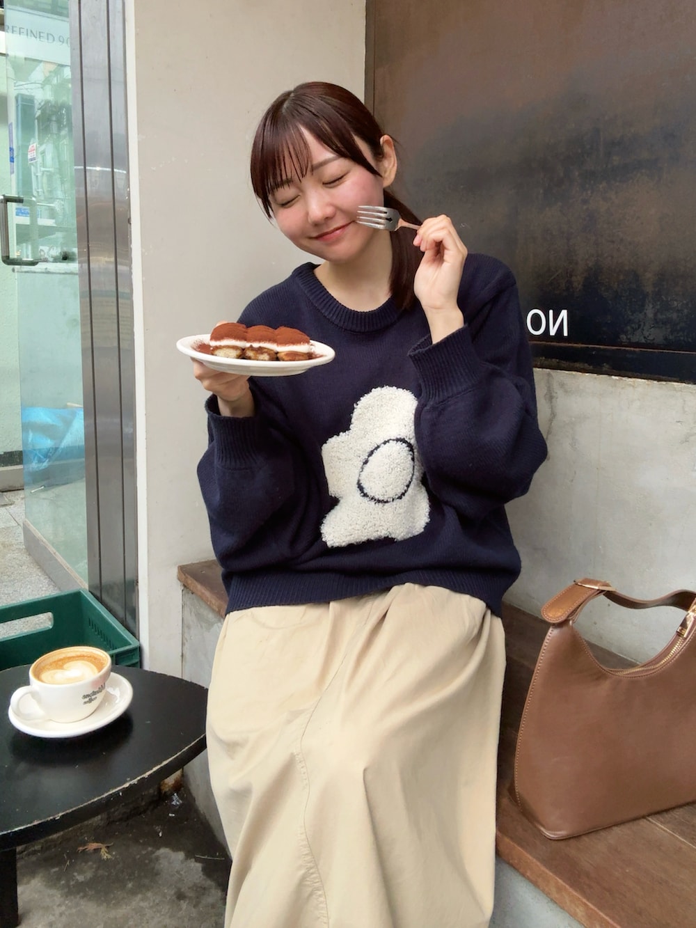 ブルー系のニット/セーター、ベージュ系のスカート、ブラック系のスニーカーを着用したレディースの春コーディネートの3枚目の写真